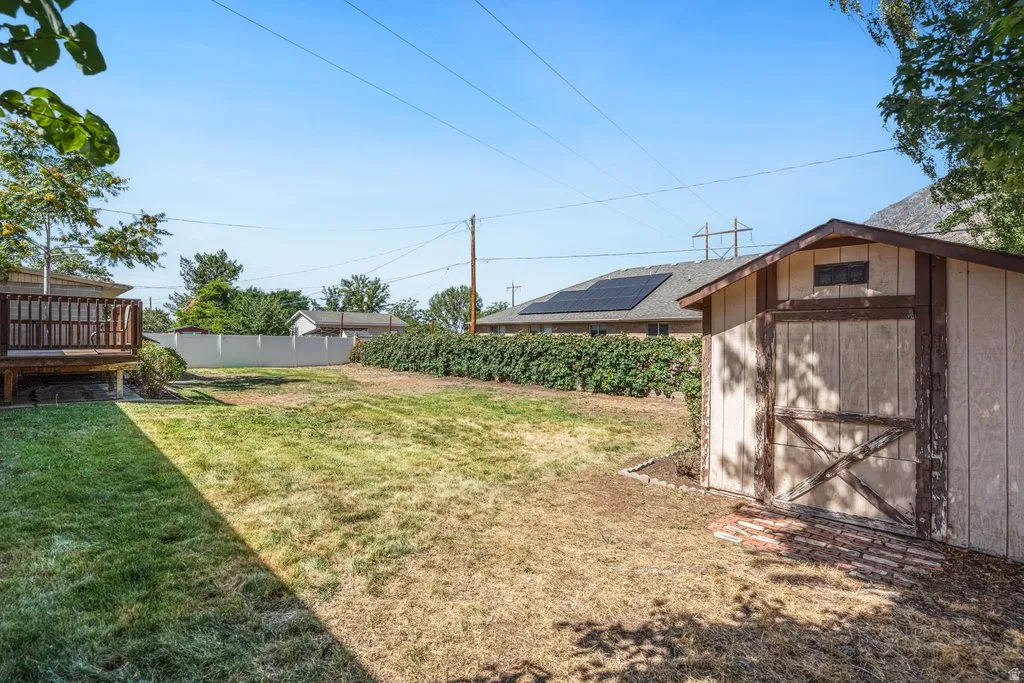 Expansive backyard featuring a wood deck, storage shed with brick paver pathway, and mature perimeter landscaping