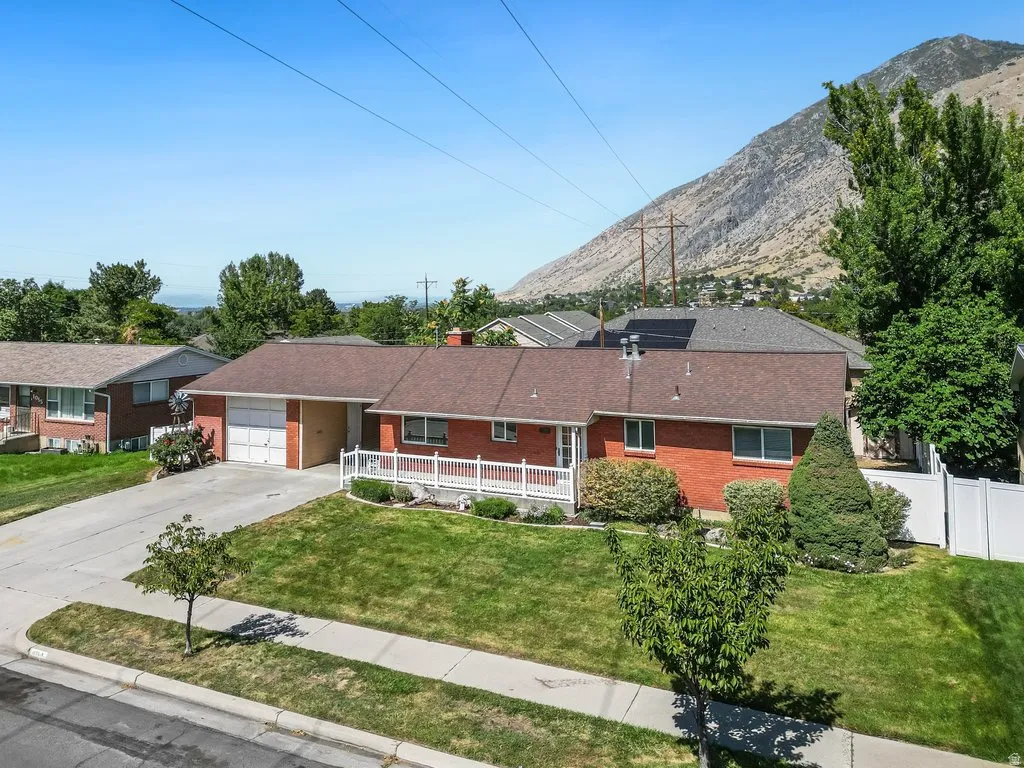 Brick exterior residence featuring an attached garage, white porch railing, and a sloped front lawn