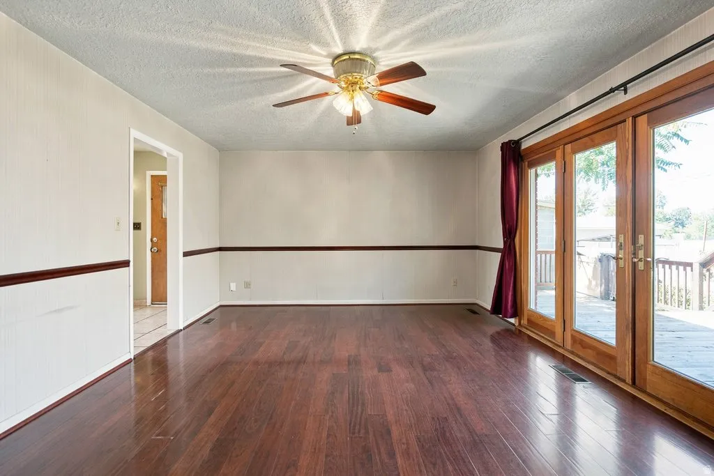 Hardwood-finish flooring, ceiling fan with integrated lighting, chair rail detailing, and full-light double doors opening to an exterior deck