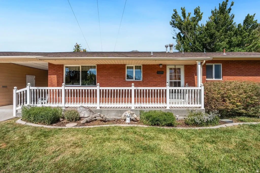 Red brick exterior with a covered porch, white railing, and a mature front lawn