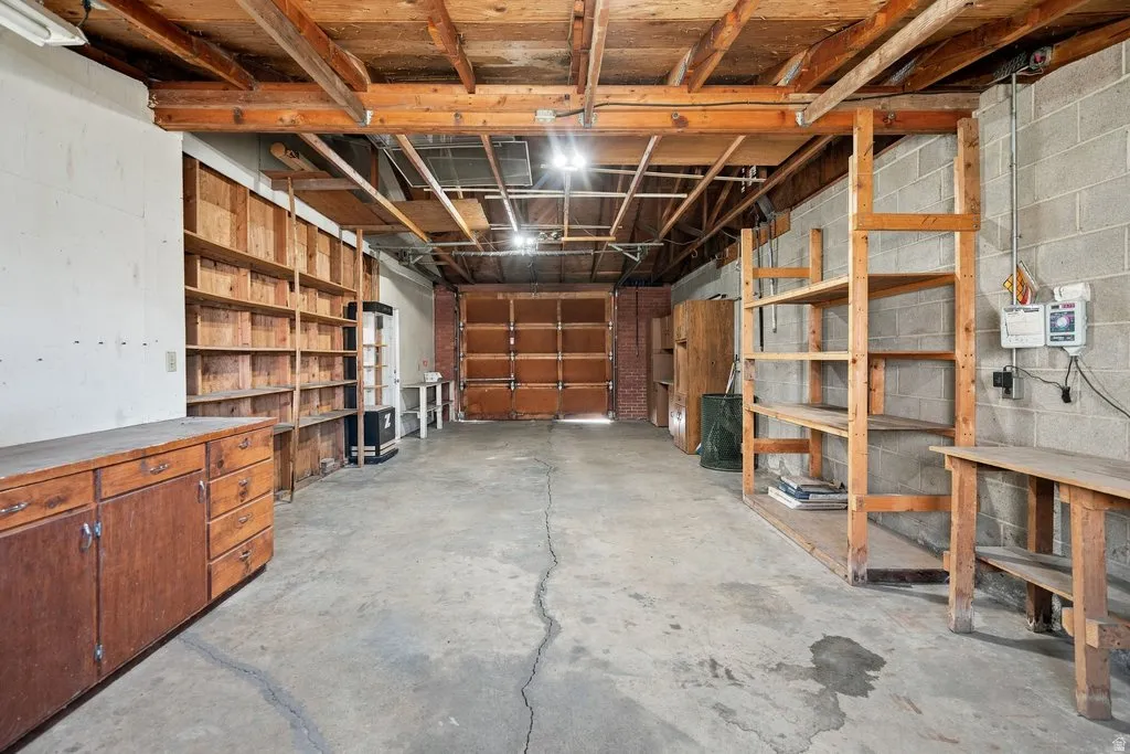 Concrete flooring, exposed wood beam ceiling, built-in wooden shelving, wooden cabinetry, and a roll-up garage door