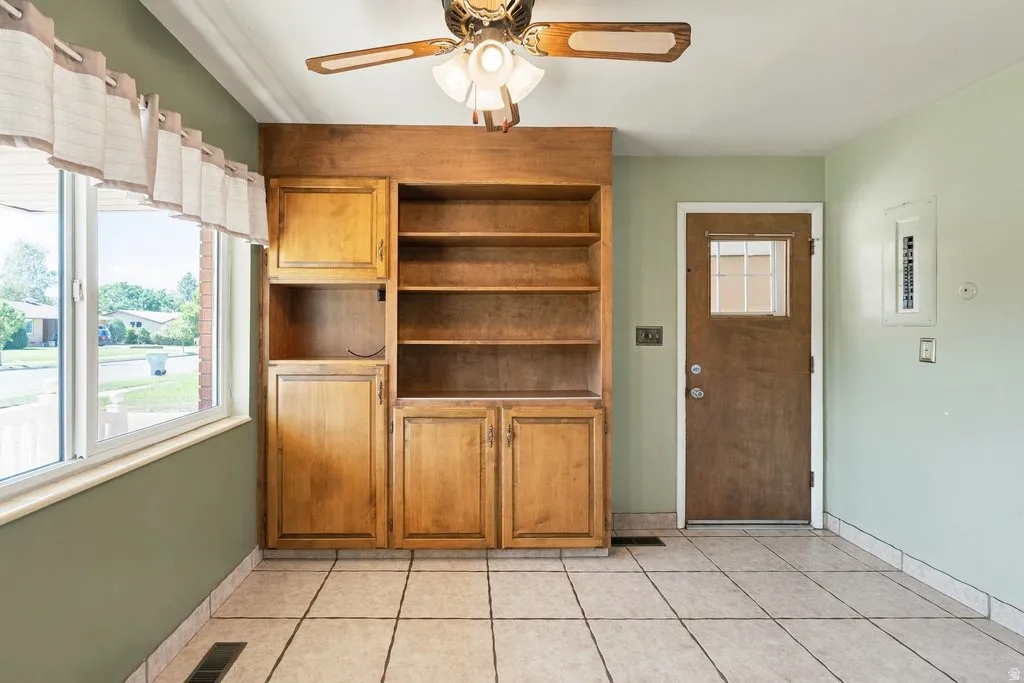 Built-in wood cabinetry with open shelving, tile flooring, ceiling fan, and painted walls
