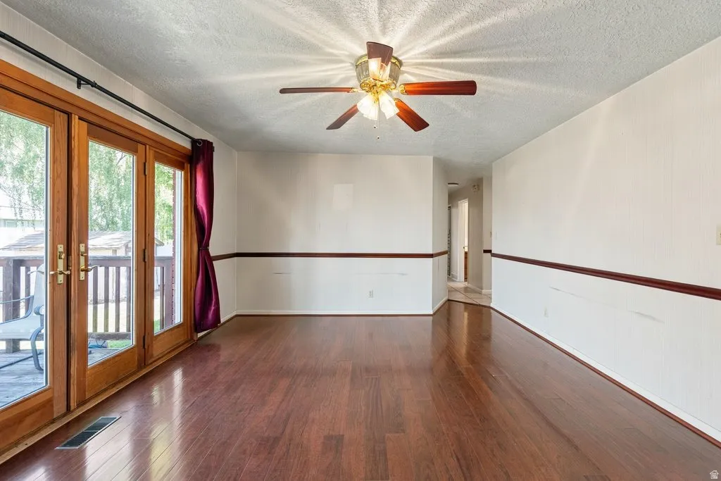 Wood-finish flooring throughout, patio access via glass-paneled double doors, ceiling fan with integrated lighting, and chair rail molding
