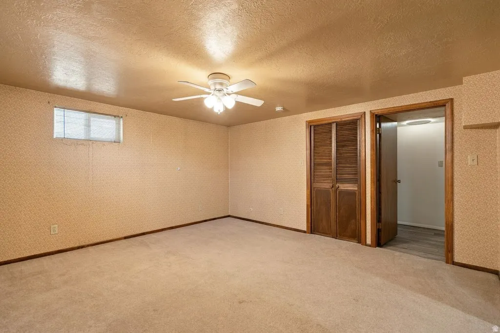 Carpeted room featuring a ceiling fan with integrated lighting, wood-finish bi-fold closet doors, and a window with blinds