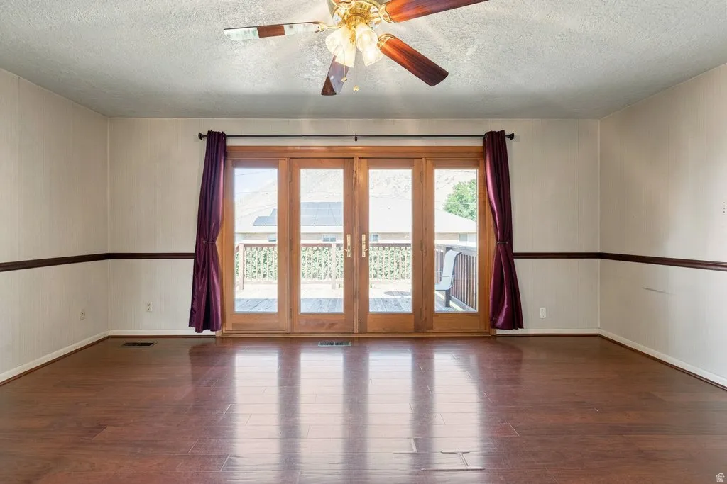 Wood-finish flooring throughout, ceiling fan with integrated lighting, and multiple paneled French doors opening to an exterior deck
