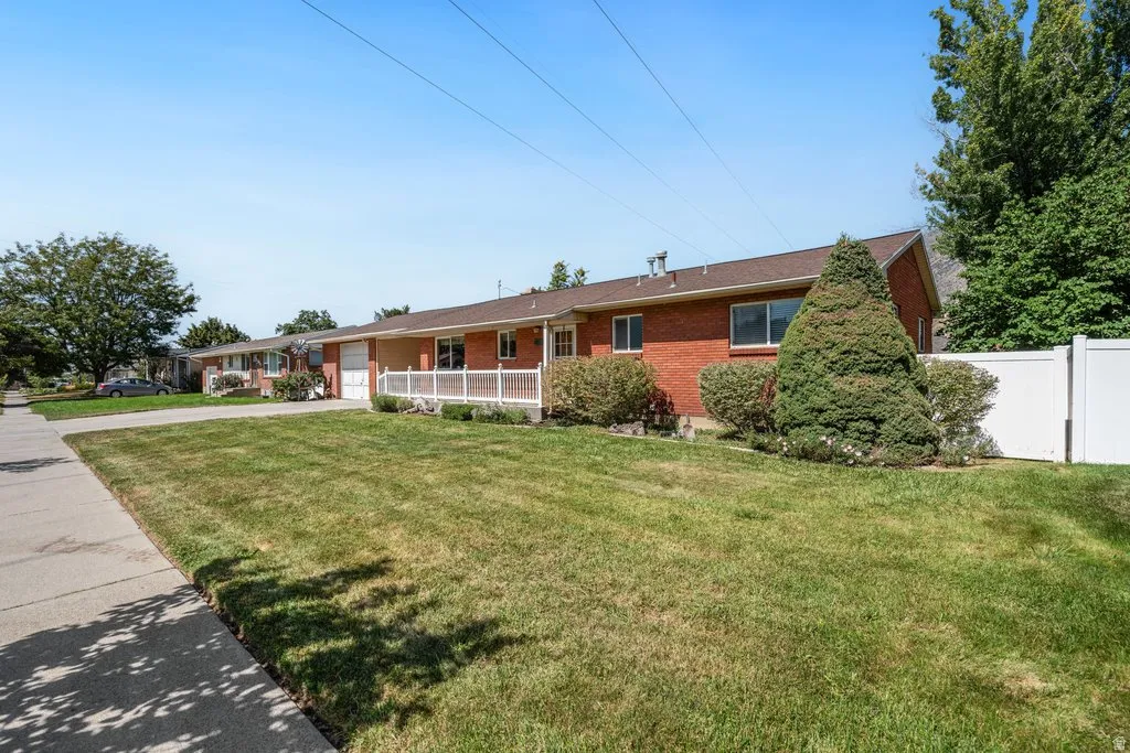 Brick exterior, white privacy fence, mature landscaping, sidewalk access, attached garage with white door
