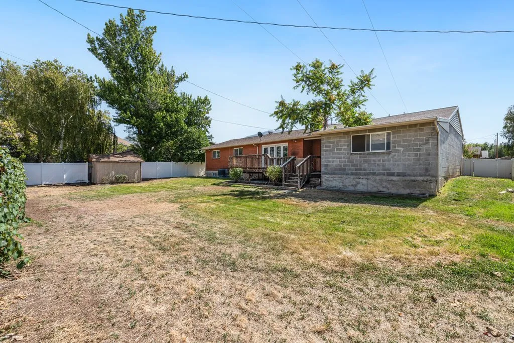 Expansive backyard featuring a privacy fence, wood deck, and a storage shed