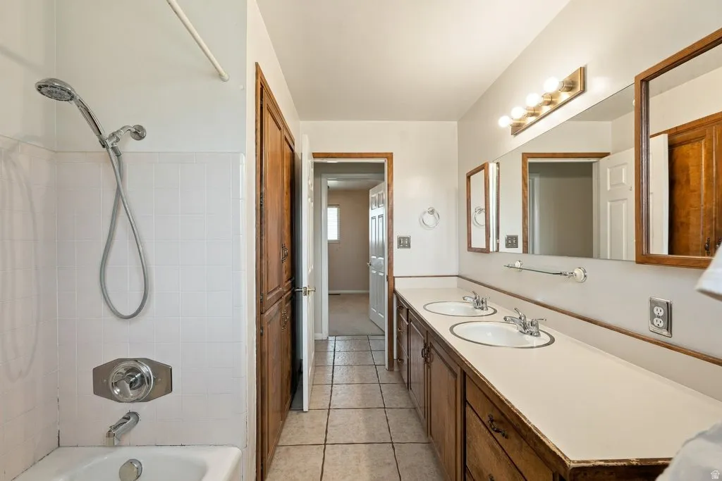 Dual vanity with integrated sinks, wood-finish cabinetry, full-width mirror, and tiled flooring