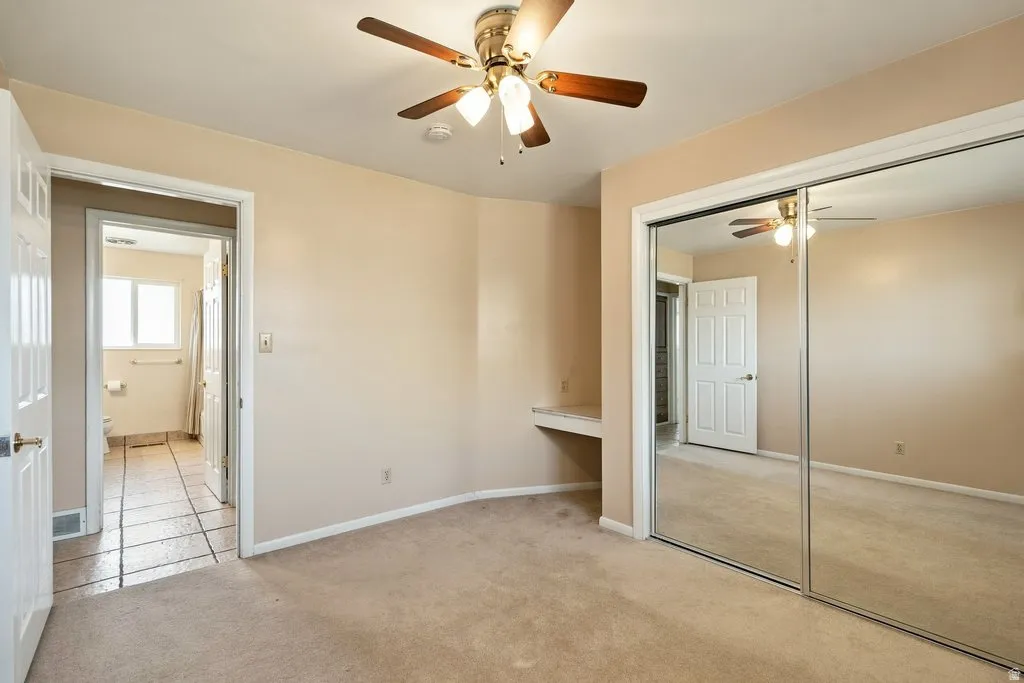 Light-toned carpeting, ceiling fan with integrated lighting, built-in desk, and mirrored sliding closet doors