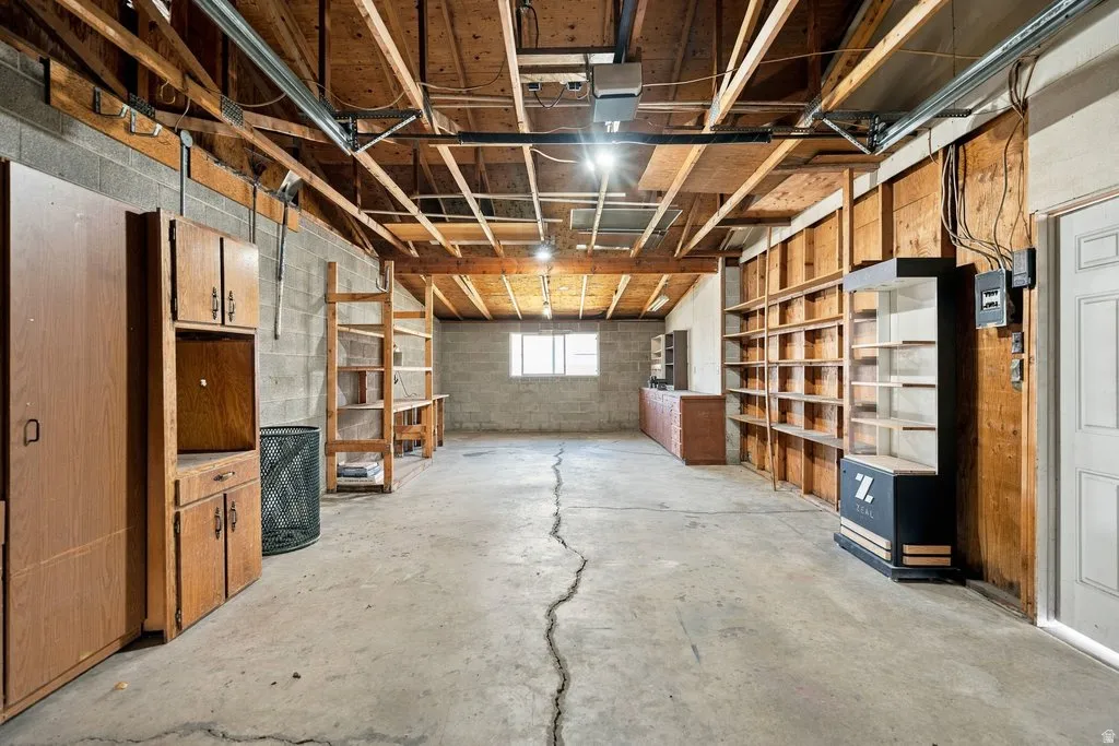 Utility space with exposed ceiling joists, concrete block walls, and built-in shelving