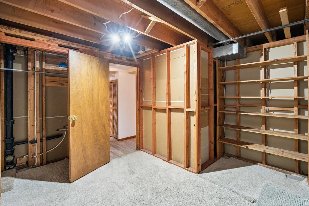 Unfinished space with exposed wood framing, wood support beams, built-in wood shelving, and carpet flooring