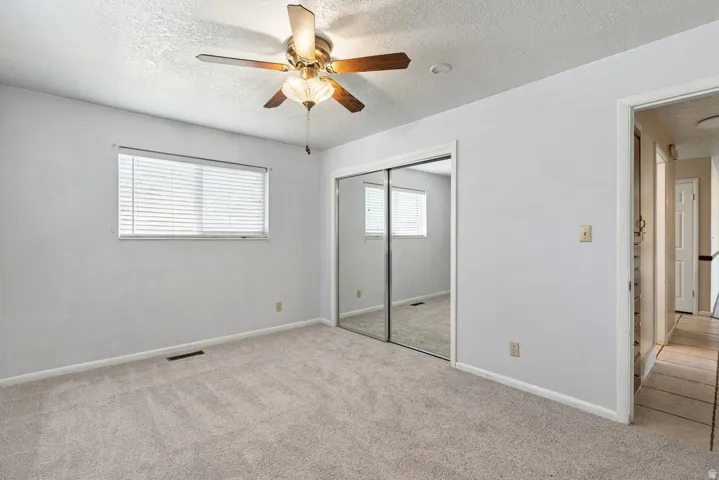 Plush carpet flooring with a ceiling fan light fixture, dual sliding mirrored closet doors, and window with horizontal blinds