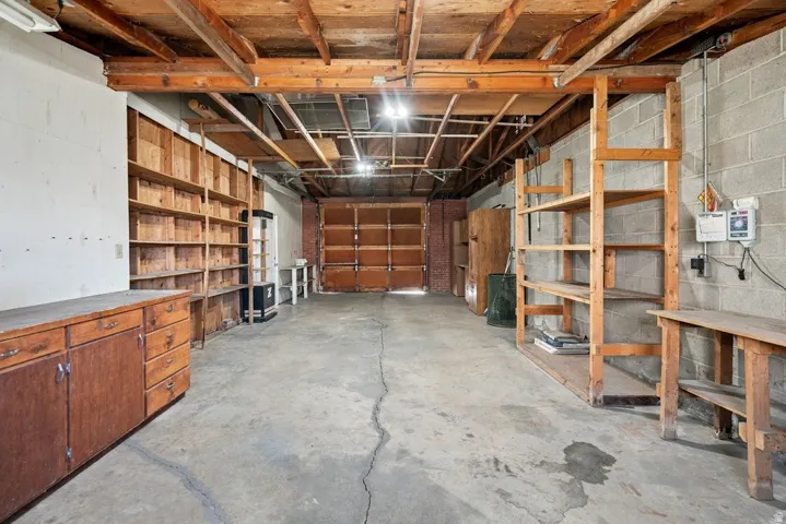 Concrete flooring, exposed wood beam ceiling, built-in wooden shelving, wooden cabinetry, and a roll-up garage door