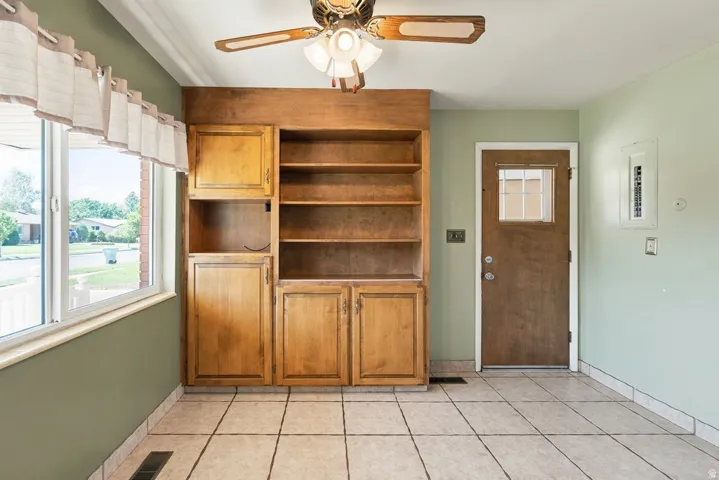 Built-in wood cabinetry with open shelving, tile flooring, ceiling fan, and painted walls