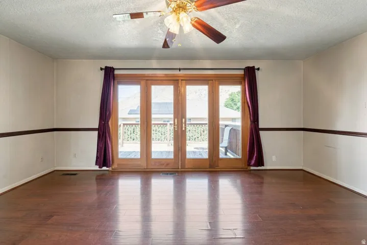 Wood-finish flooring throughout, ceiling fan with integrated lighting, and multiple paneled French doors opening to an exterior deck