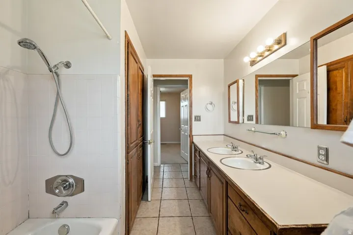Dual vanity with integrated sinks, wood-finish cabinetry, full-width mirror, and tiled flooring