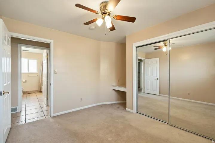 Light-toned carpeting, ceiling fan with integrated lighting, built-in desk, and mirrored sliding closet doors