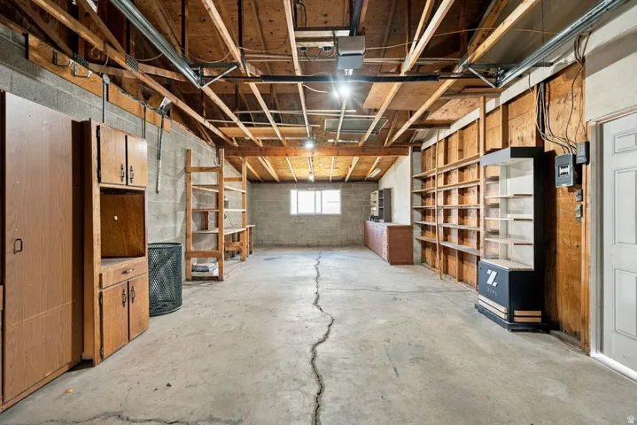 Utility space with exposed ceiling joists, concrete block walls, and built-in shelving
