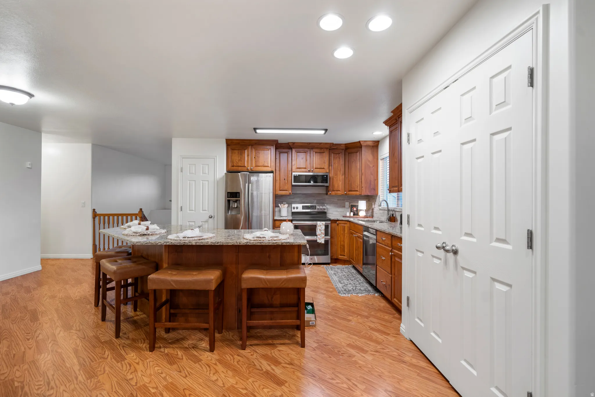 Kitchen featuring wood-finish flooring, a central island with a granite-style countertop, wood cabinetry, stainless steel appliances, and recessed lighting