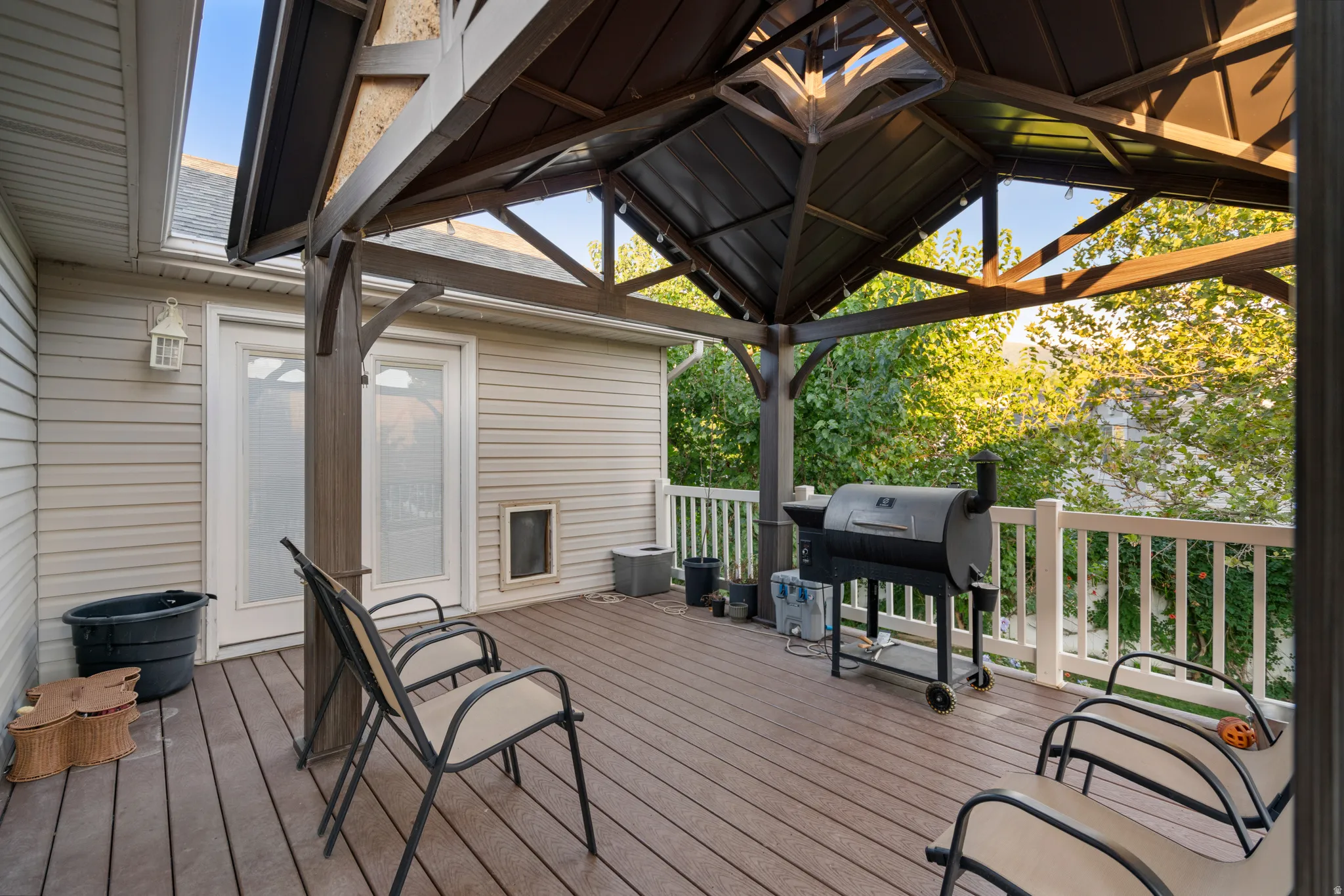 Wood-finish deck with a built-in gazebo, featuring white railing, light-colored siding, and white double doors with frosted glass