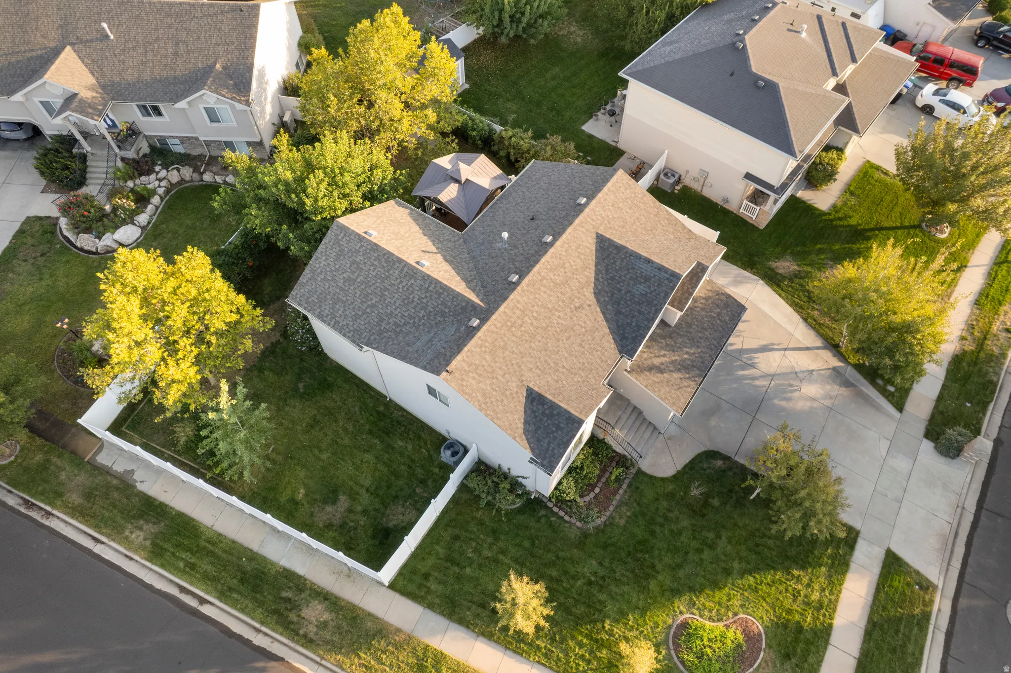 Gable rooflines, white exterior siding, concrete driveway, front yard landscaping, and mature trees
