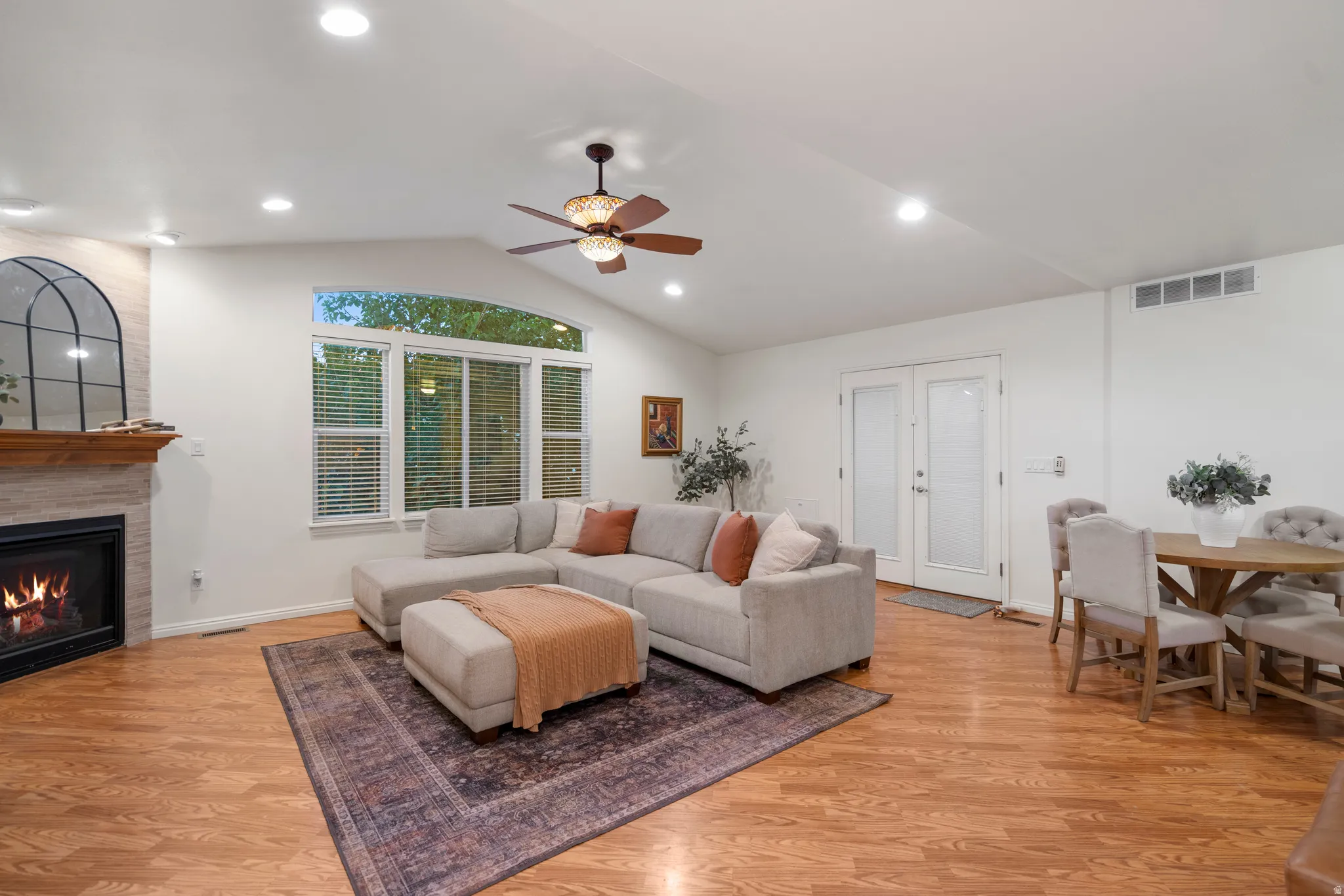 Vaulted ceilings with recessed lighting, wood-finish flooring, stone fireplace with a wood mantle, large picture windows, and double French doors with frosted glass