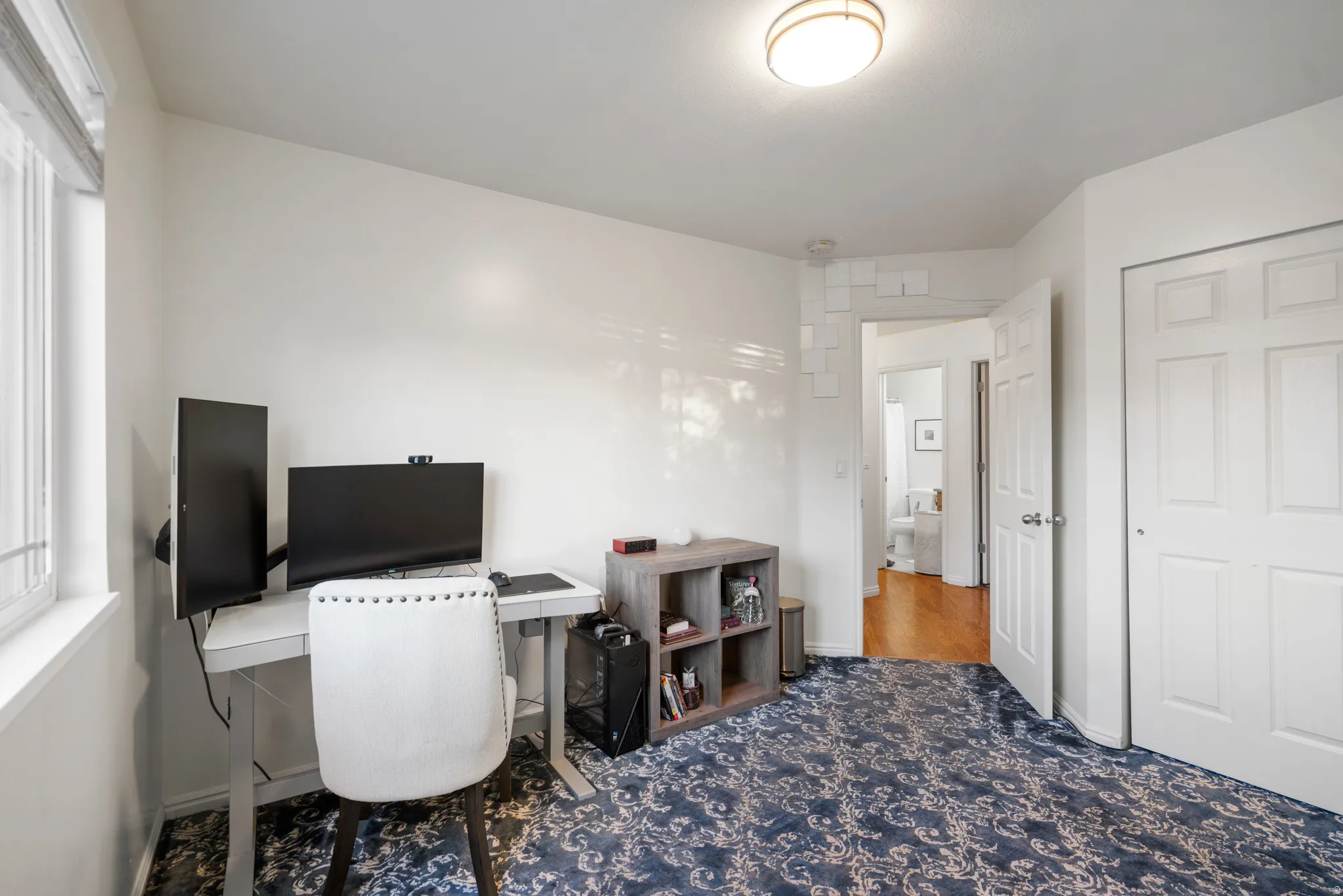 White walls, recessed window, patterned carpet, flush mount ceiling light, and a white paneled door