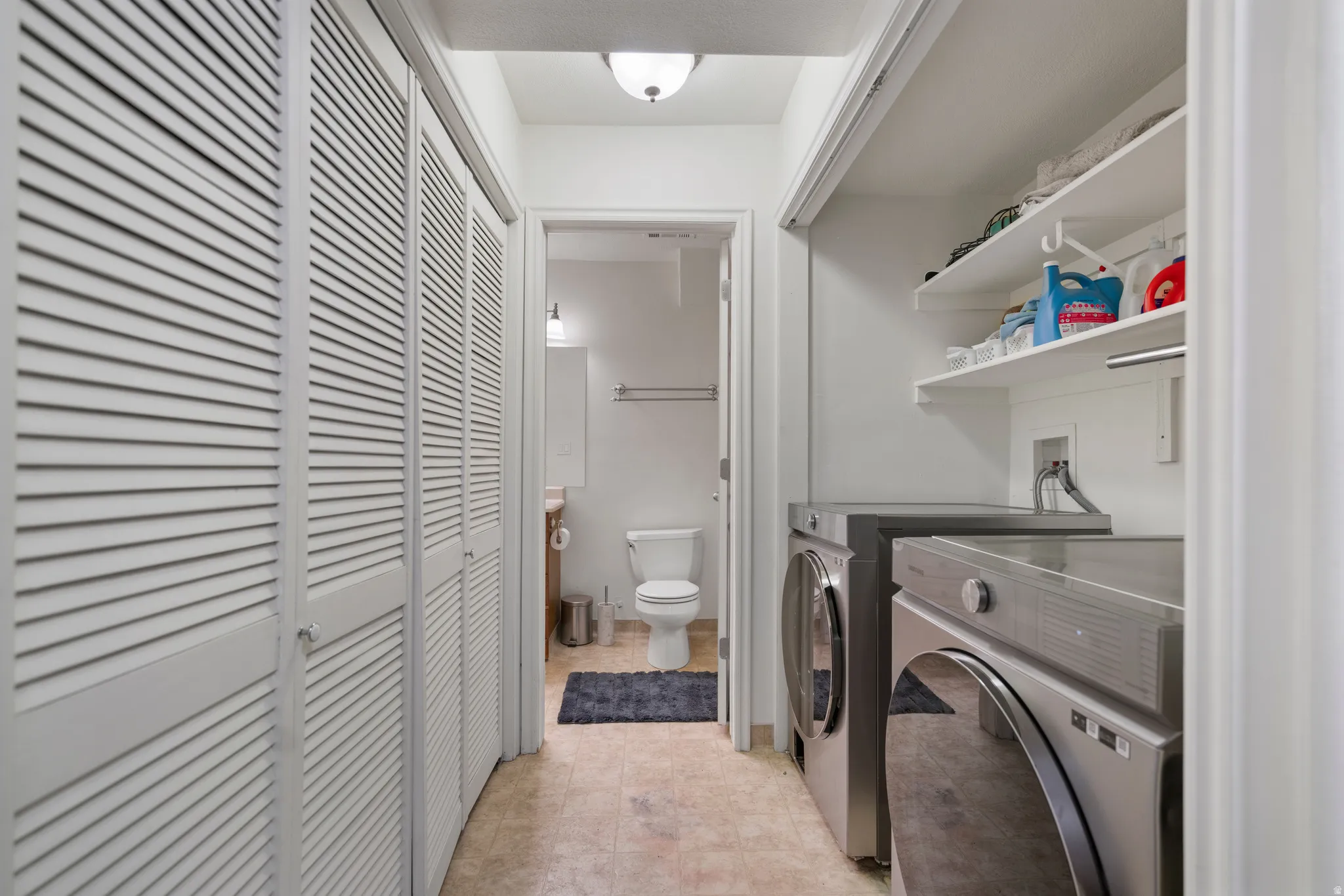 Laundry area with built-in shelving, front-loading washer and dryer, and louvered bifold closet doors