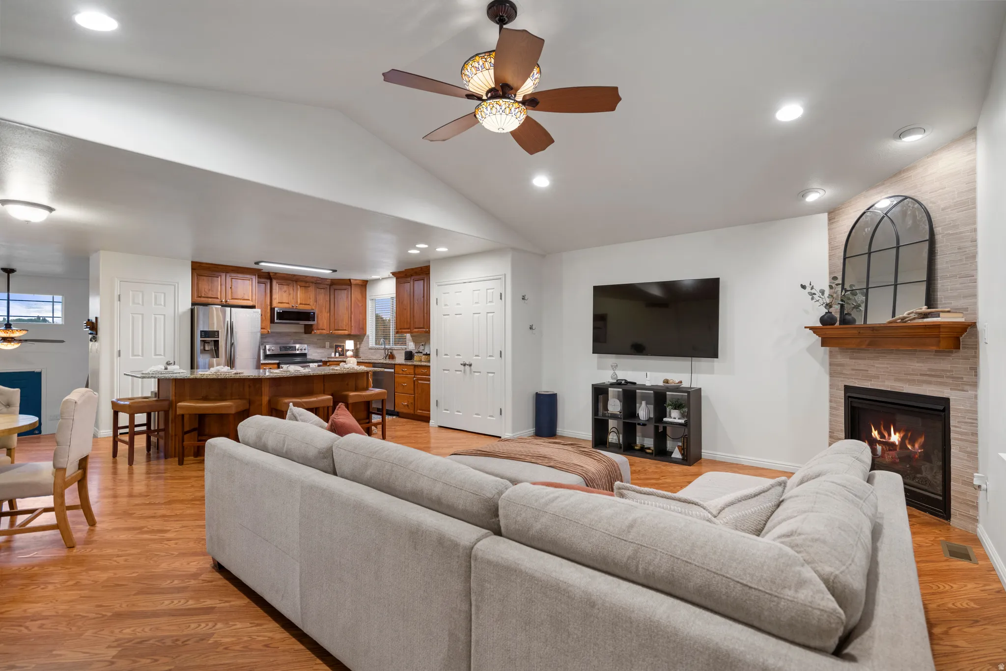 Vaulted ceiling with a ceiling fan, recessed lighting, wood-finish flooring, built-in fireplace with a mantel, and a kitchen with wood cabinetry