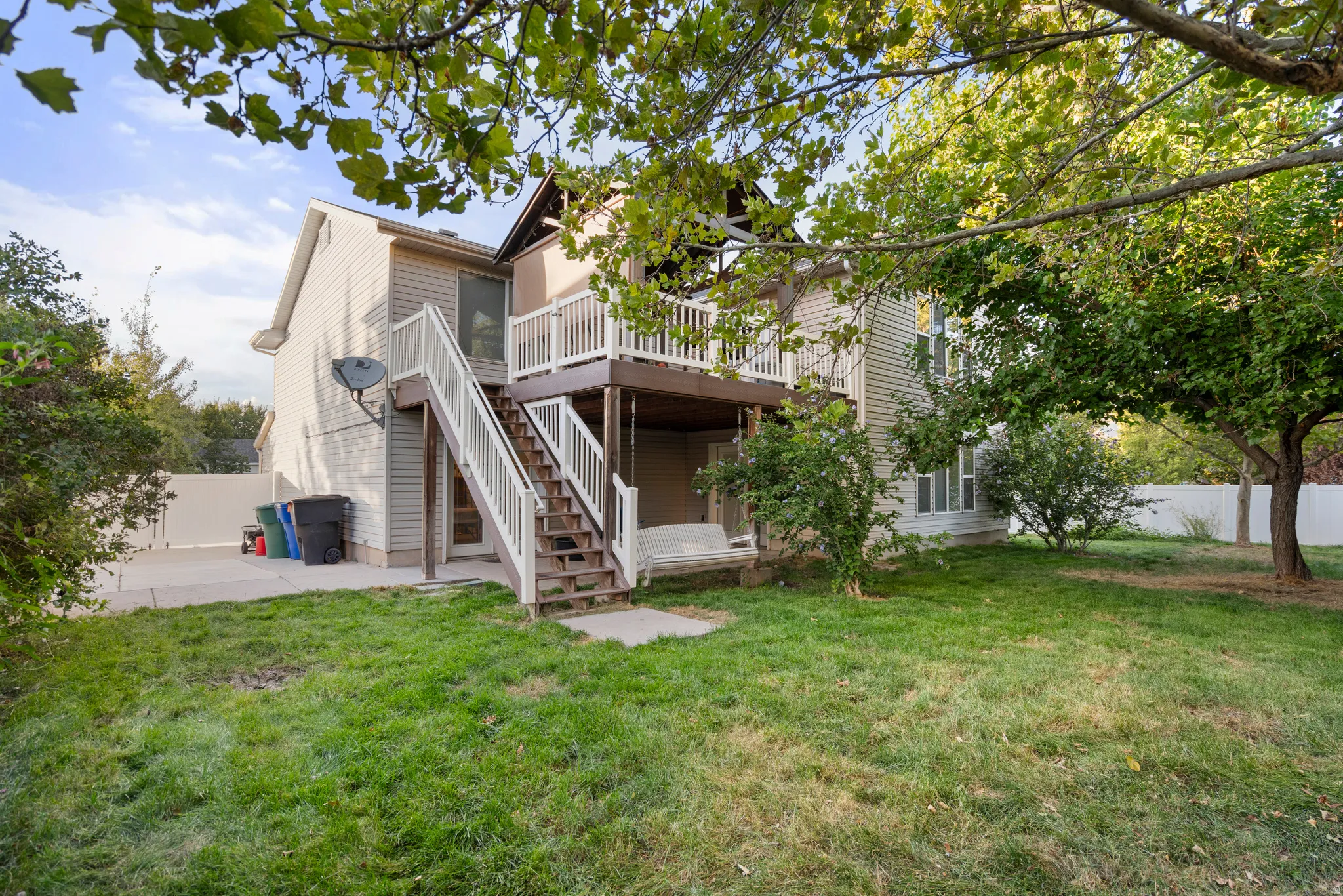 Two-story property with siding exterior, upper-level wood deck with white railings, lower-level patio, and a manicured lawn