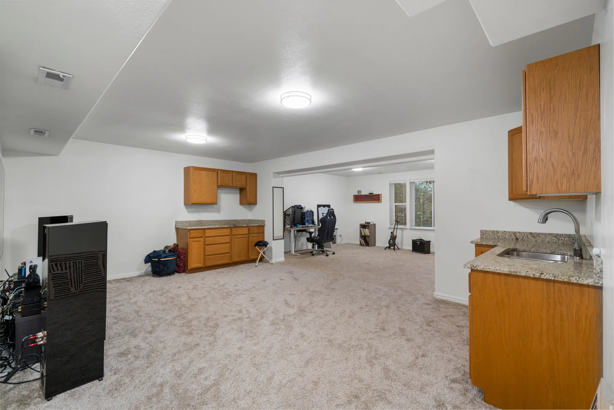 Spacious finished lower level with carpeted flooring, built-in cabinetry, stone countertops, and a wet bar with an undermount sink