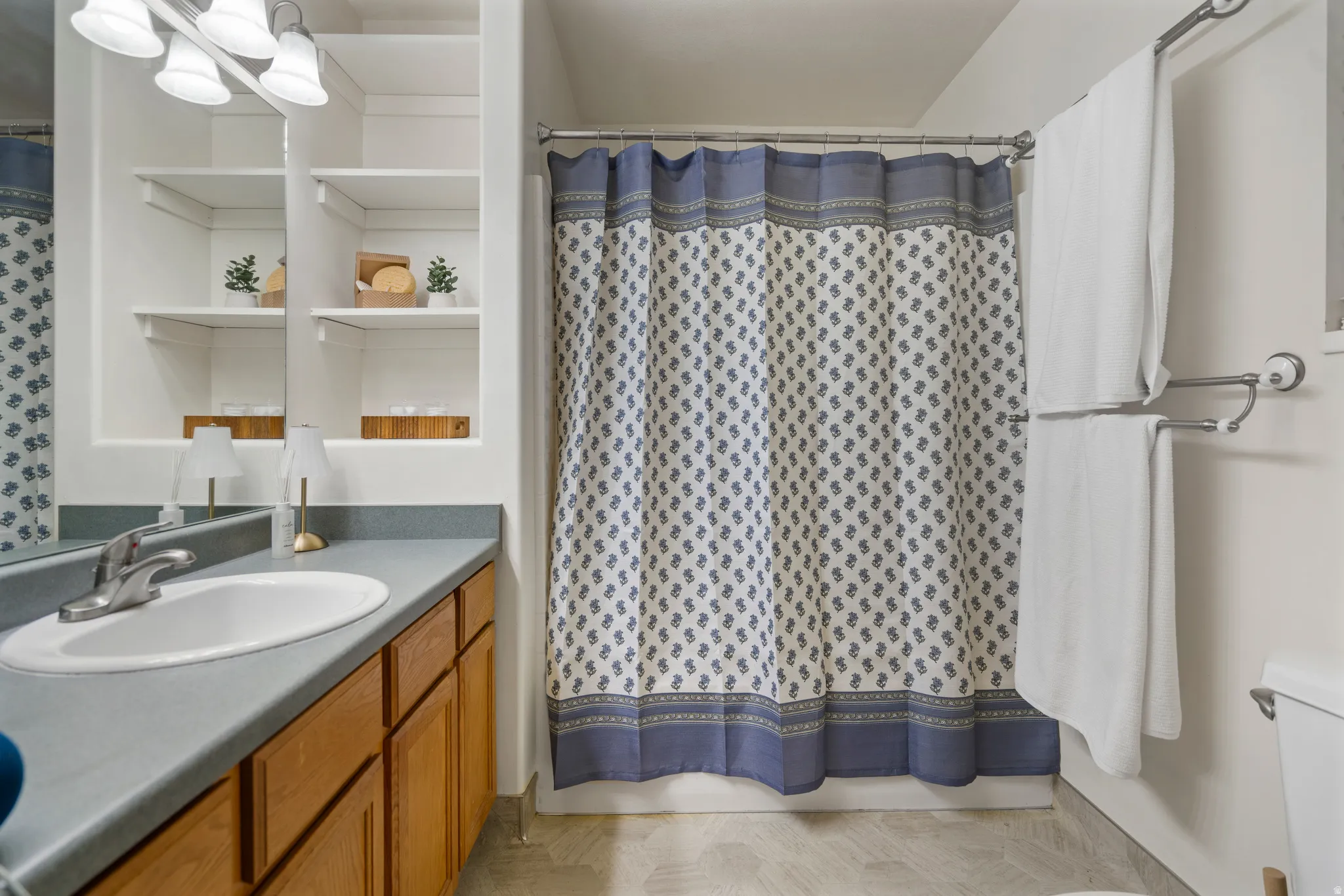 Primary Vanity with wood-finish cabinetry, built-in shelving, mounted light fixture, and a shower with a curtain rod