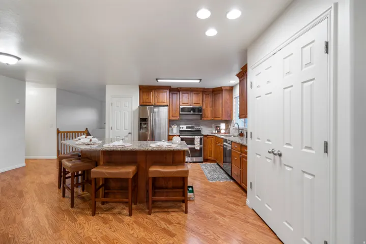 Kitchen featuring wood-finish flooring, a central island with a granite-style countertop, wood cabinetry, stainless steel appliances, and recessed lighting