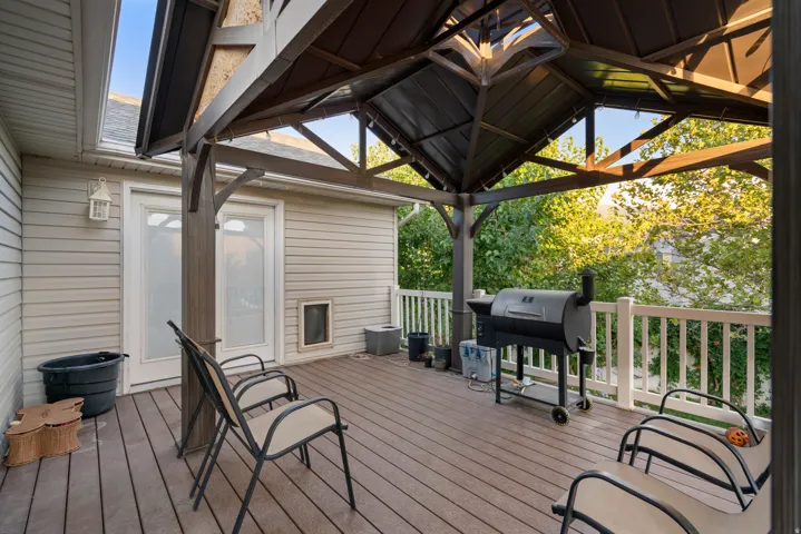 Wood-finish deck with a built-in gazebo, featuring white railing, light-colored siding, and white double doors with frosted glass