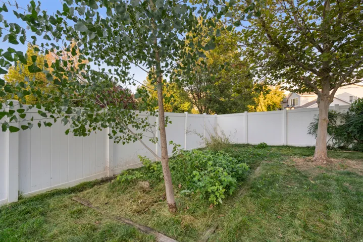 Expansive backyard featuring a white privacy fence, mature trees, and natural landscaping
