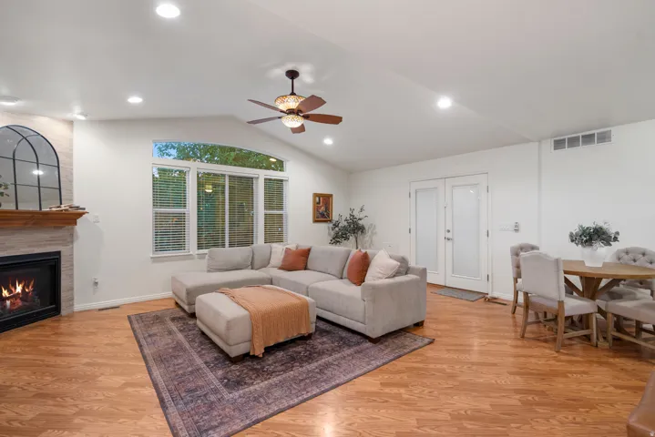 Vaulted ceilings with recessed lighting, wood-finish flooring, stone fireplace with a wood mantle, large picture windows, and double French doors with frosted glass