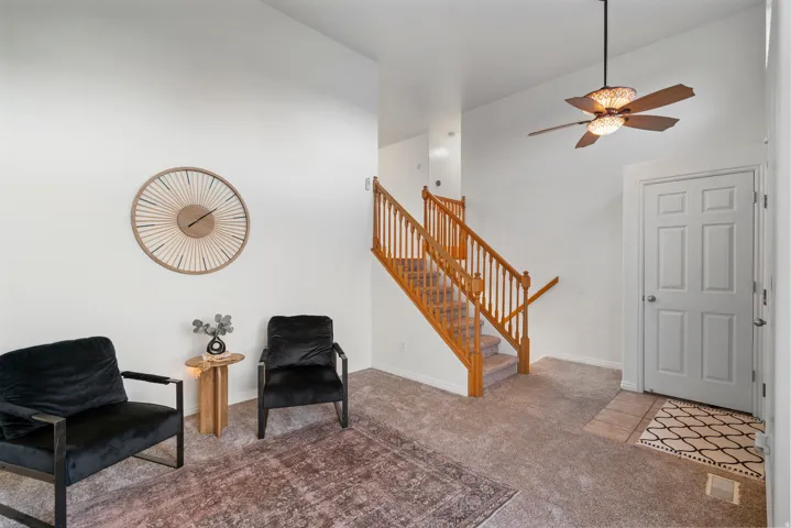 Vaulted ceiling, ceiling fan with integrated lighting, wood staircase with balusters, paneled interior door, and neutral carpeting