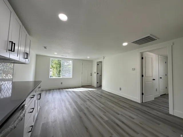 White shaker cabinetry with black hardware, mosaic tile backsplash, recessed lighting, wood-finish flooring, and a white paneled door
