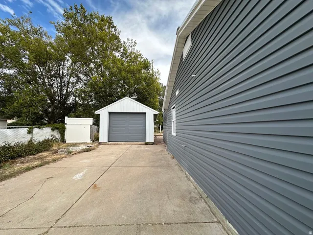 Detached garage with roll-up door, concrete driveway, and gray horizontal siding on the main structure