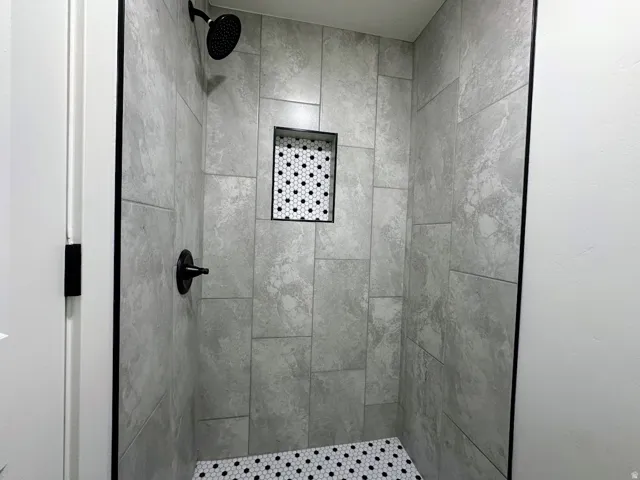 Shower enclosure with large format grey tile, black hexagonal mosaic tile floor, and a recessed niche with matching mosaic tile