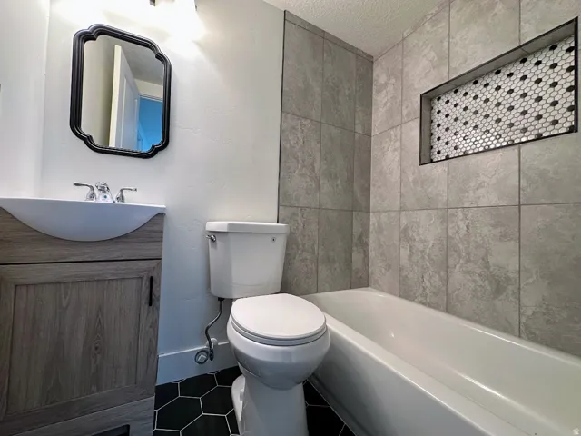 Bathroom featuring a white bathtub, tiled shower surround with an inset niche, wood-finish vanity with a vessel sink, and hexagonal floor tiling