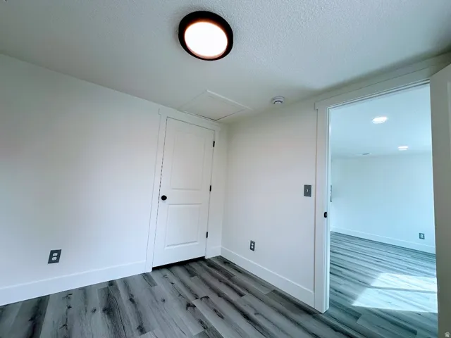 Wood-finish flooring throughout, white interior doors with black hardware, flush mount ceiling light, and recessed lighting in the adjacent room