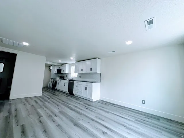 Spacious area featuring wood-finish flooring, recessed lighting, white cabinetry, dark countertops, and a tiled backsplash