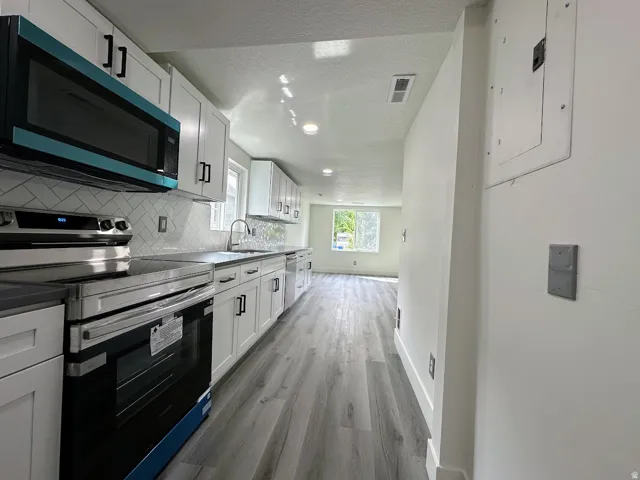 Modern kitchen featuring white cabinetry with black hardware, stainless steel appliances, a white subway tile backsplash, and light wood-finish flooring
