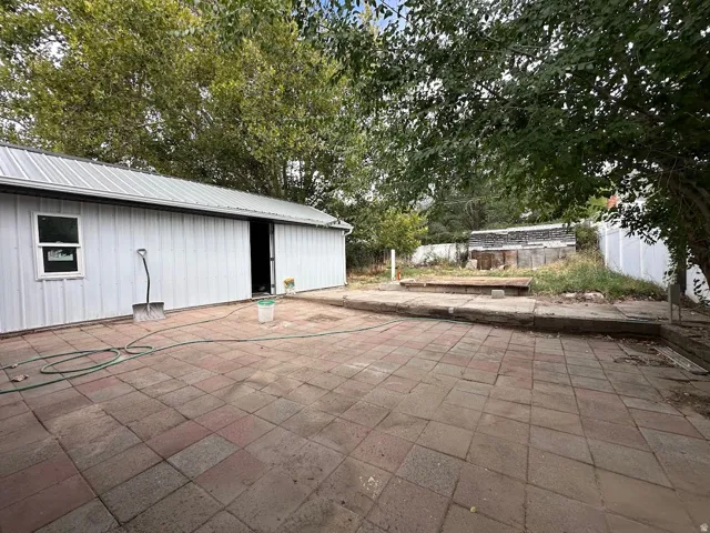 Expansive paved patio area featuring a detached utility building with a metal roof and a sliding door
