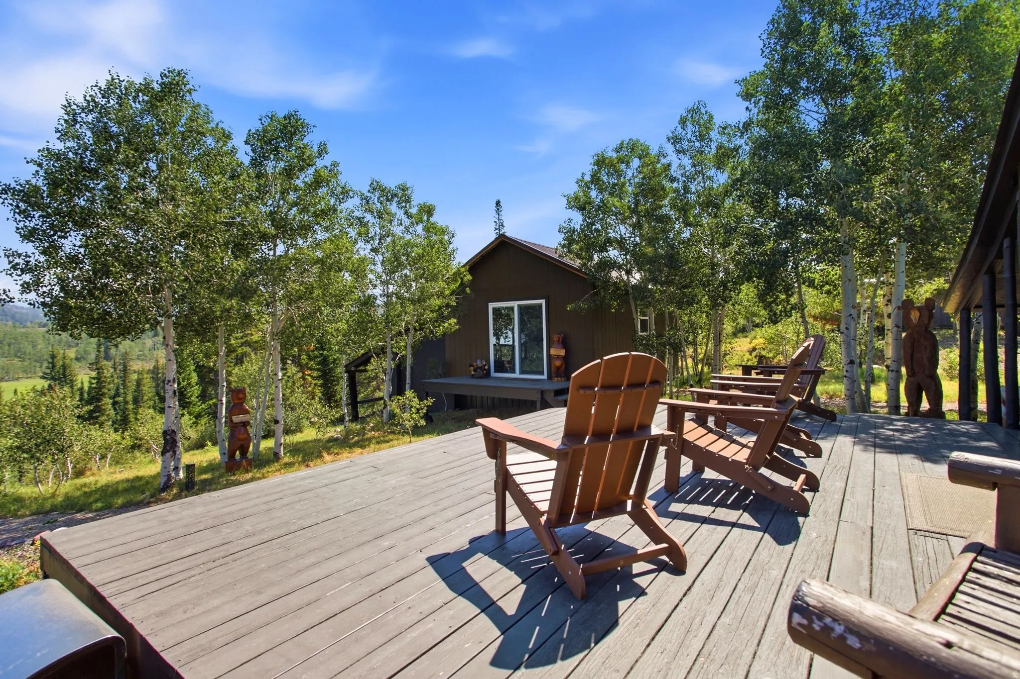 Expansive composite deck surrounded by mature trees, featuring a brown exterior dwelling with a sliding glass door