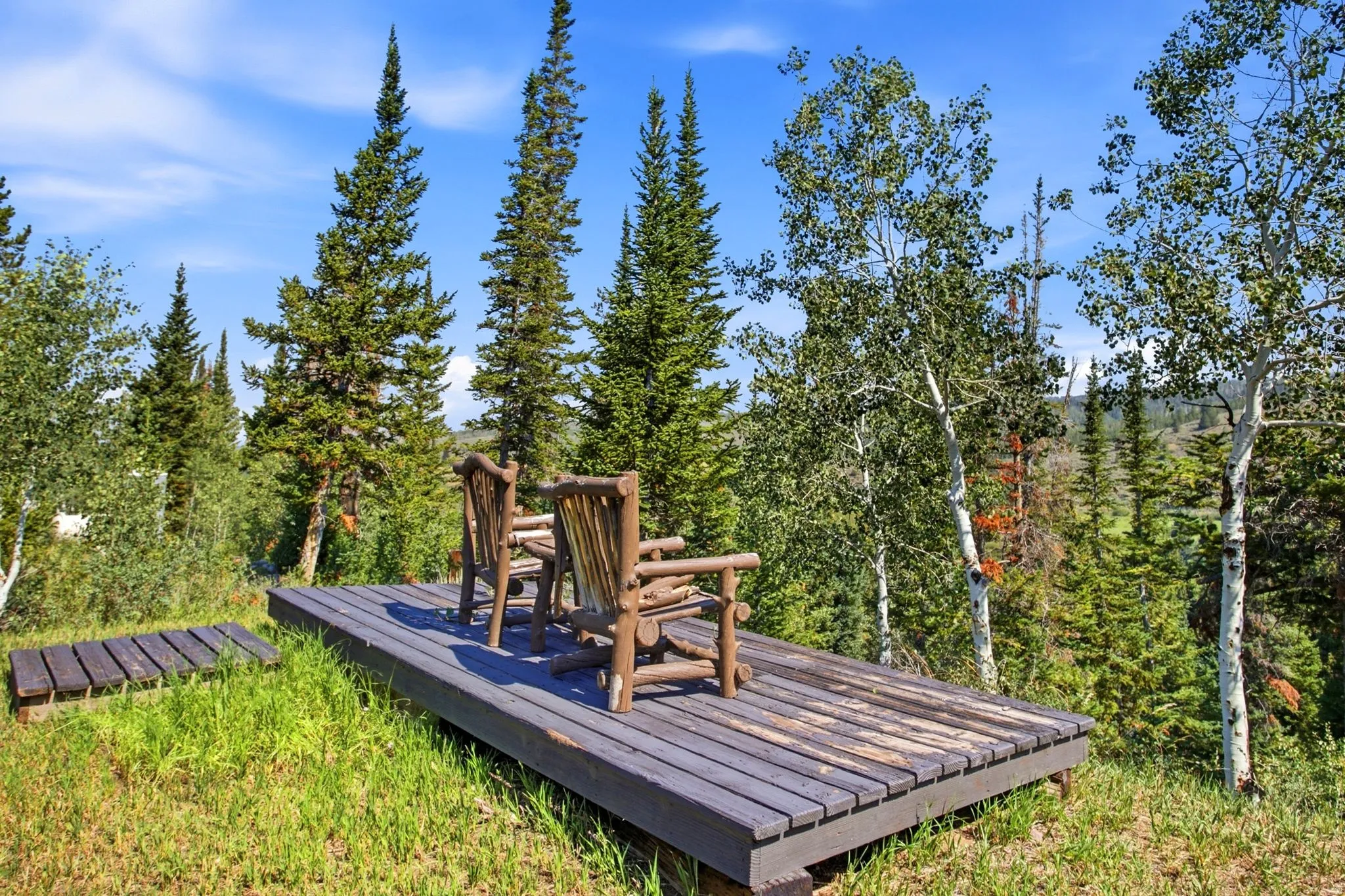 Outdoor wood deck with natural wood chairs, surrounded by evergreen and deciduous trees