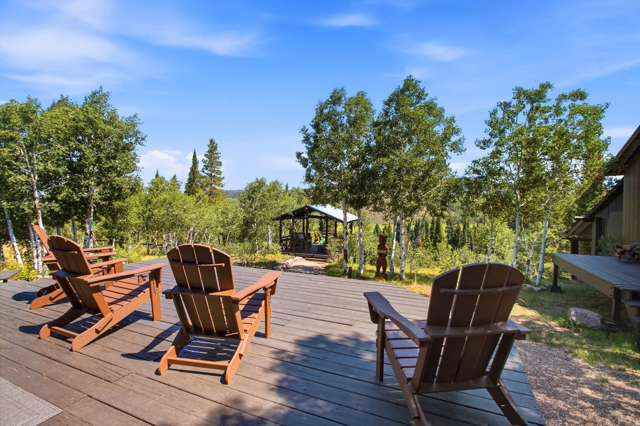 Expansive outdoor decking, gazebo structure, and natural landscaping with mature trees