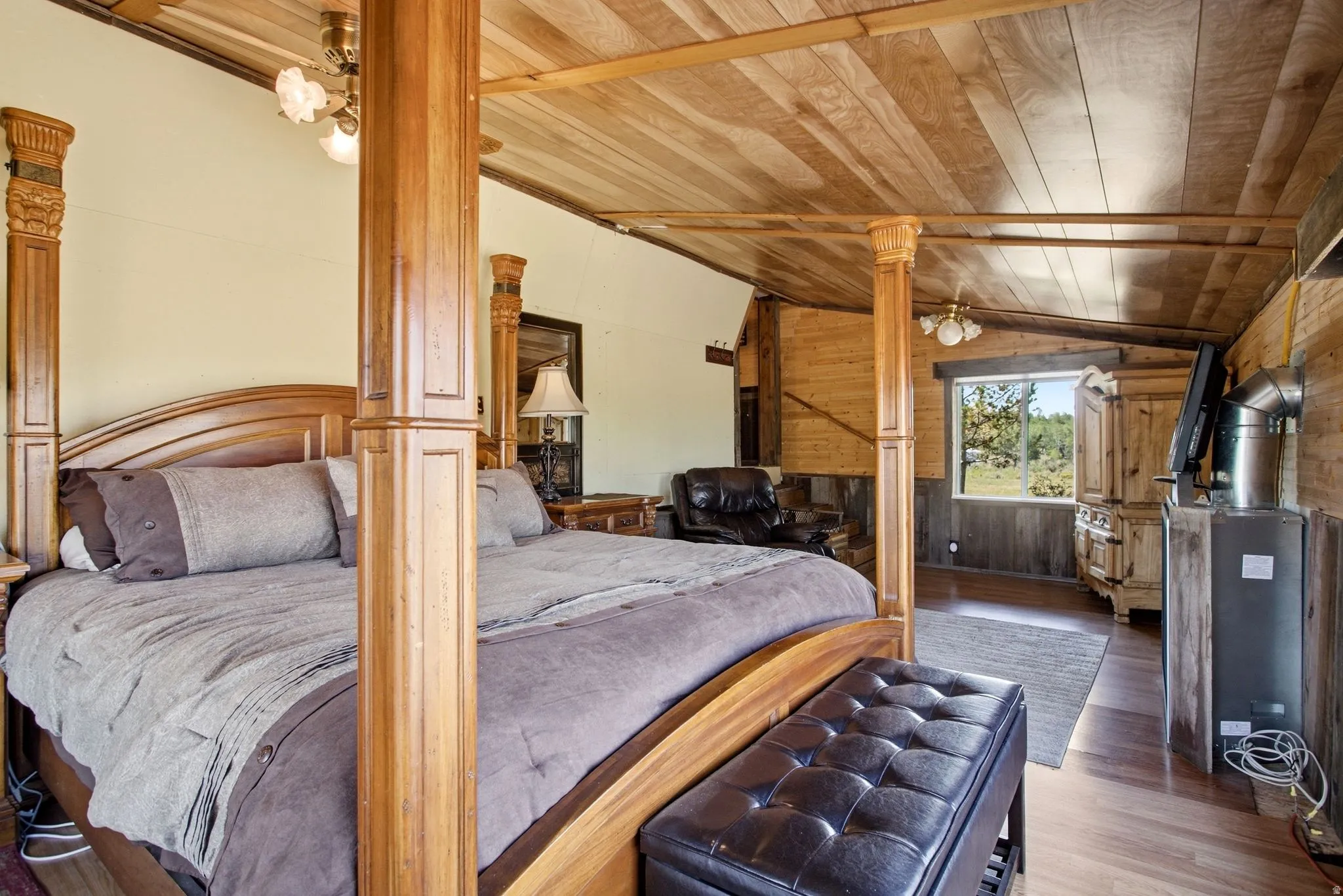 Vaulted wood-paneled ceiling, wood-finish flooring, accent wood paneling, wood window trim, and a ceiling fan with integrated lighting