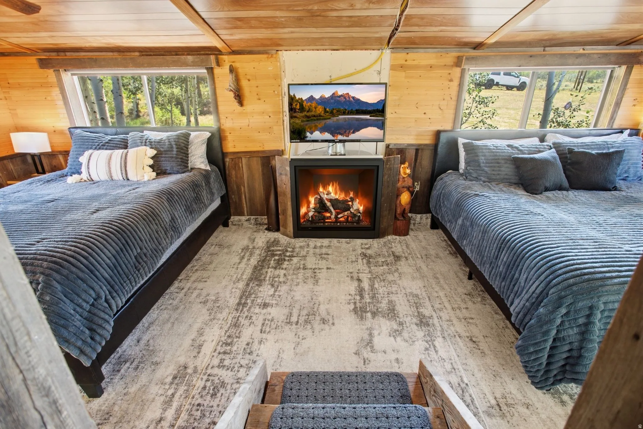 Wood-paneled walls and ceiling, wood-finish flooring, two large windows, and a built-in electric fireplace